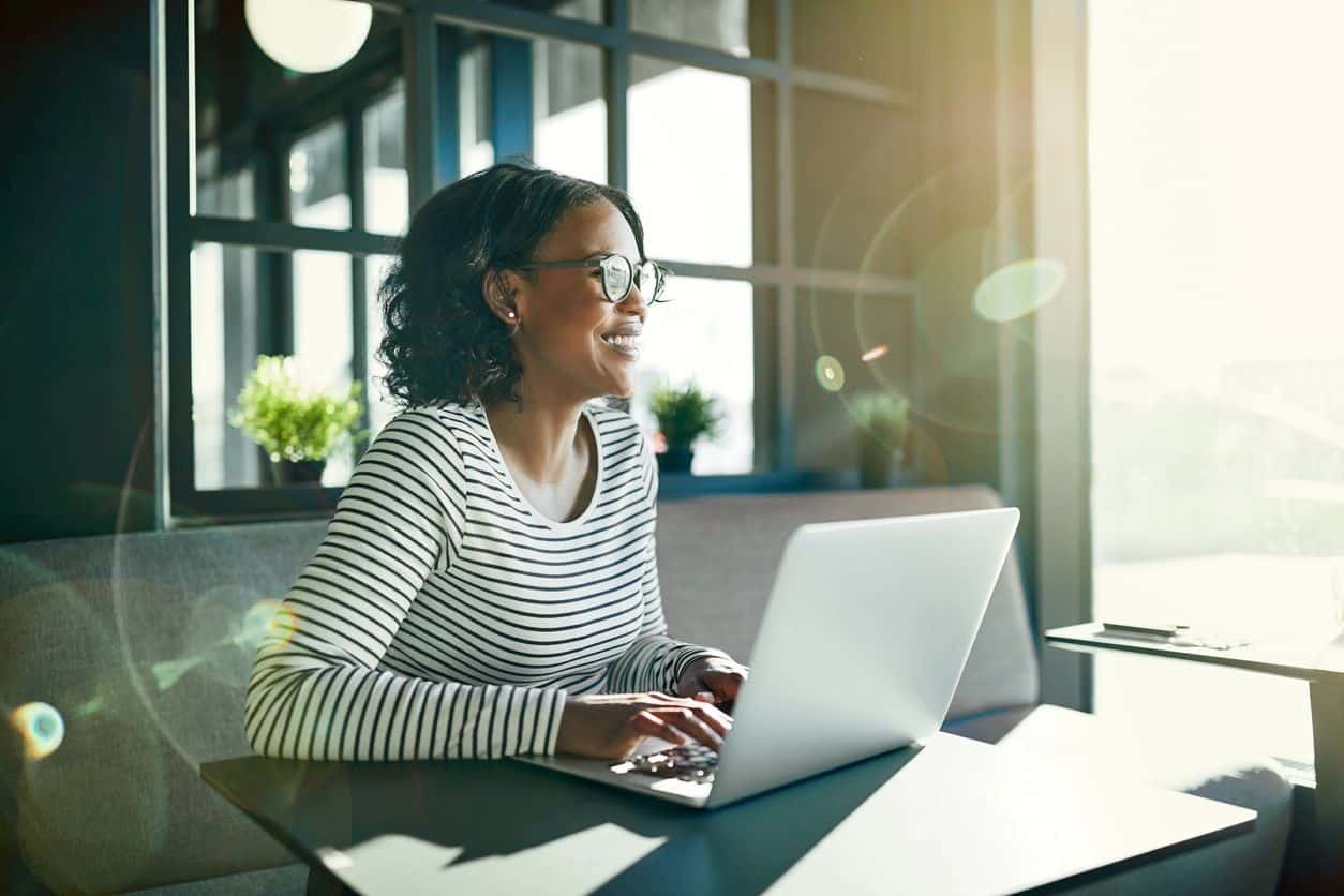 Person with glasses smiling while using laptop at table